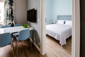 A hotel room with a bed, a TV mounted on the wall, and a dining area with chairs and a table. - Cracow Rentals Zacisze (Kraków)
