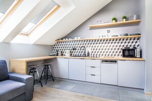 A modern kitchen with skylights, a wooden countertop, white cabinets, and a grey sofa. - Cracow Rentals Zacisze (Kraków)
