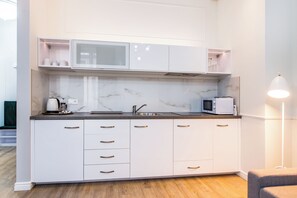 A modern kitchen with white cabinets, a marble backsplash, and a microwave. - Cracow Rentals Zacisze (Kraków)