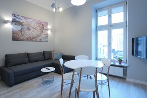 A modern living room with a grey sofa, a round dining table, and a TV mounted on the wall. - Cracow Rentals Zacisze (Kraków)