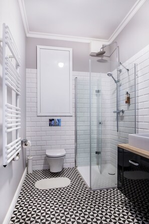 A modern bathroom with a glass-enclosed shower, a white toilet, and a sink with a wooden countertop. - Cracow Rentals Zacisze (Kraków)