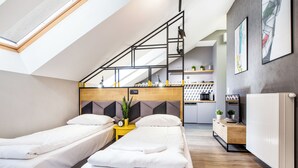 Quarto de hotel moderno com duas camas de solteiro, claraboia, cozinha e vista para a cidade.