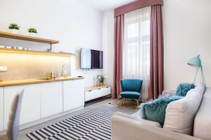 A modern living room with a sofa, a chair, a TV, and a kitchen area with a counter and cabinets. - Cracow Rentals Zacisze (Kraków)