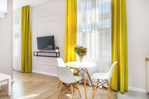 A modern living room with a flat-screen TV mounted on the wall, a round dining table with white chairs, and a vase of flowers. - Cracow Rentals Zacisze (Kraków)