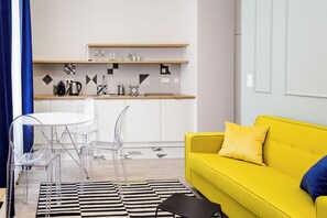 A modern living room with a yellow sofa, a black and white striped rug, and a clear glass table with chairs. - Cracow Rentals Zacisze (Kraków)