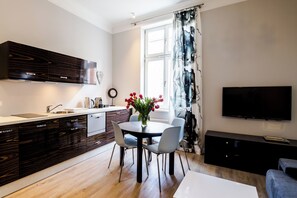 A modern kitchen with dark wood cabinetry, a white countertop, and a dining area with a round table and chairs. - Cracow Rentals Zacisze (Kraków)