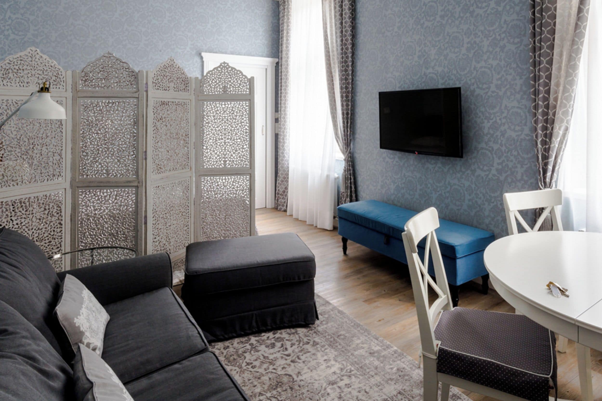 A modern living room with a sofa, ottoman, blue bench, white table, and a TV mounted on the wall.
