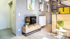 Uma sala de estar moderna com uma TV sobre um armário de madeira, uma obra de arte na parede e uma pequena mesa com um vaso de flores.