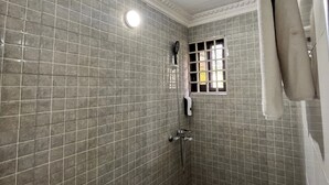 Pequeño espacio de ducha con azulejos, un cabezal de ducha de mano, una ventana con barrotes y un perchero.