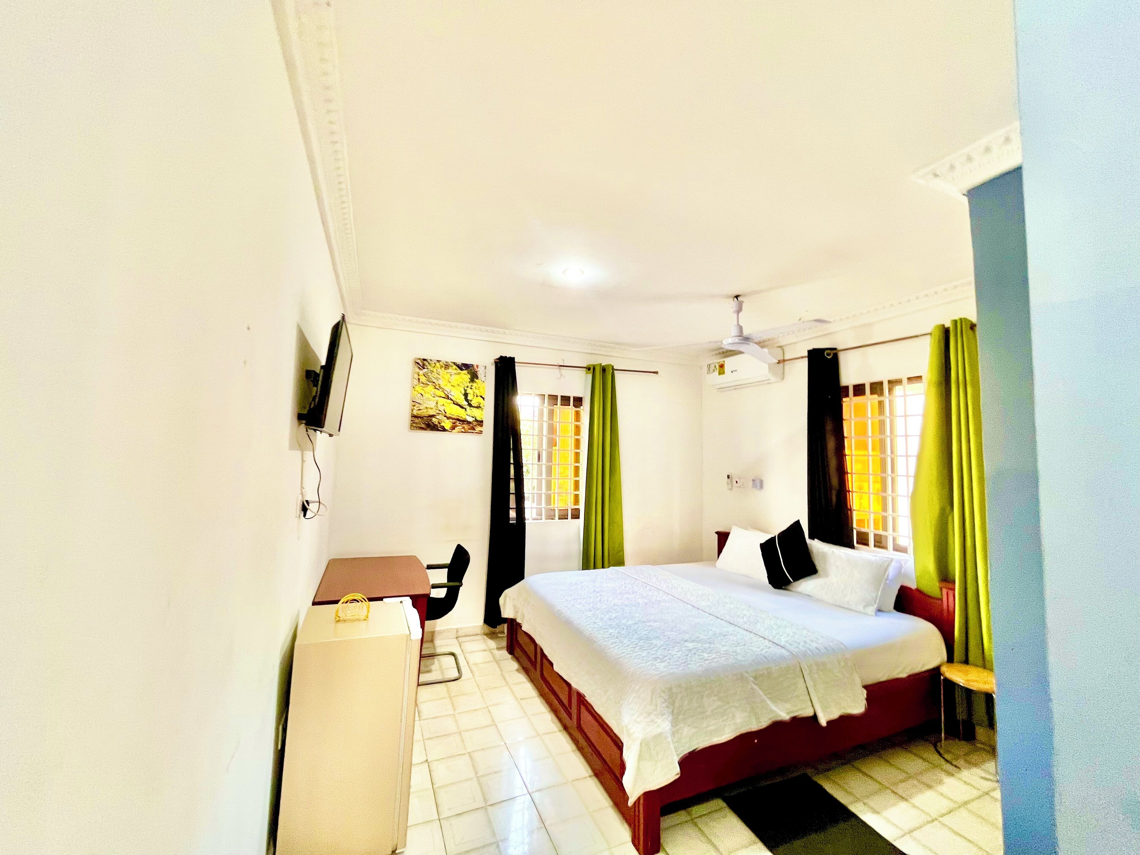 Une chambre d’hôtel avec un lit, un bureau, une chaise, une télévision et une fenêtre avec des rideaux.