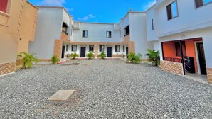 Un patio con suelo de grava, rodeado por edificios con fachadas de blanco y beige, y pequeñas plantas en macetas.