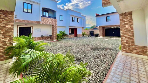 Un edificio residencial moderno con un patio interior, que presenta una combinación de muros de ladrillo y enlucido, varios balcones y un camino de entrada de grava.