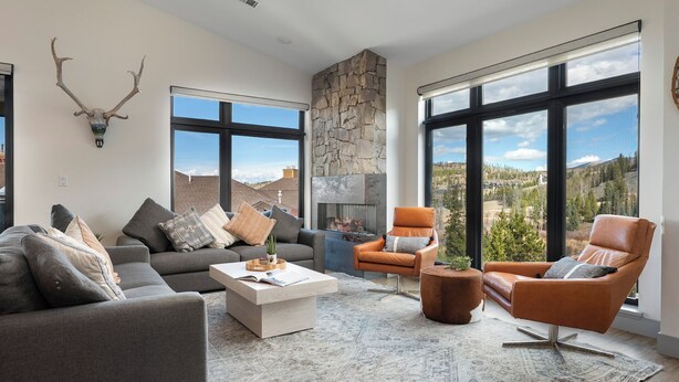 Uma sala de estar moderna com lareira de pedra, janelas amplas com vista para as montanhas e um espaço de estar aconchegante.