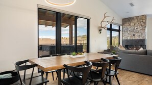 Uma área de jantar moderna com uma mesa de madeira e cadeiras pretas, uma lareira de pedra e uma janela grande com vista para o exterior.