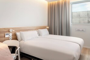 Une chambre d’hôtel avec un lit double, une table de chevet avec une lampe, une chaise et une fenêtre avec des rideaux.