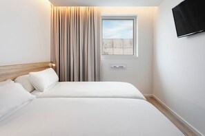 Una habitación de hotel moderna con una cama, un ventanal con cortinas, un televisor montado y un aire acondicionado instalado en la pared.