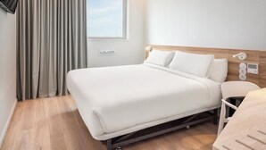 A modern hotel room with a bed, a bedside table, a lamp, a window with curtains, and a wooden floor. - B&B Hotel Vila Do Conde (Vila do Conde)