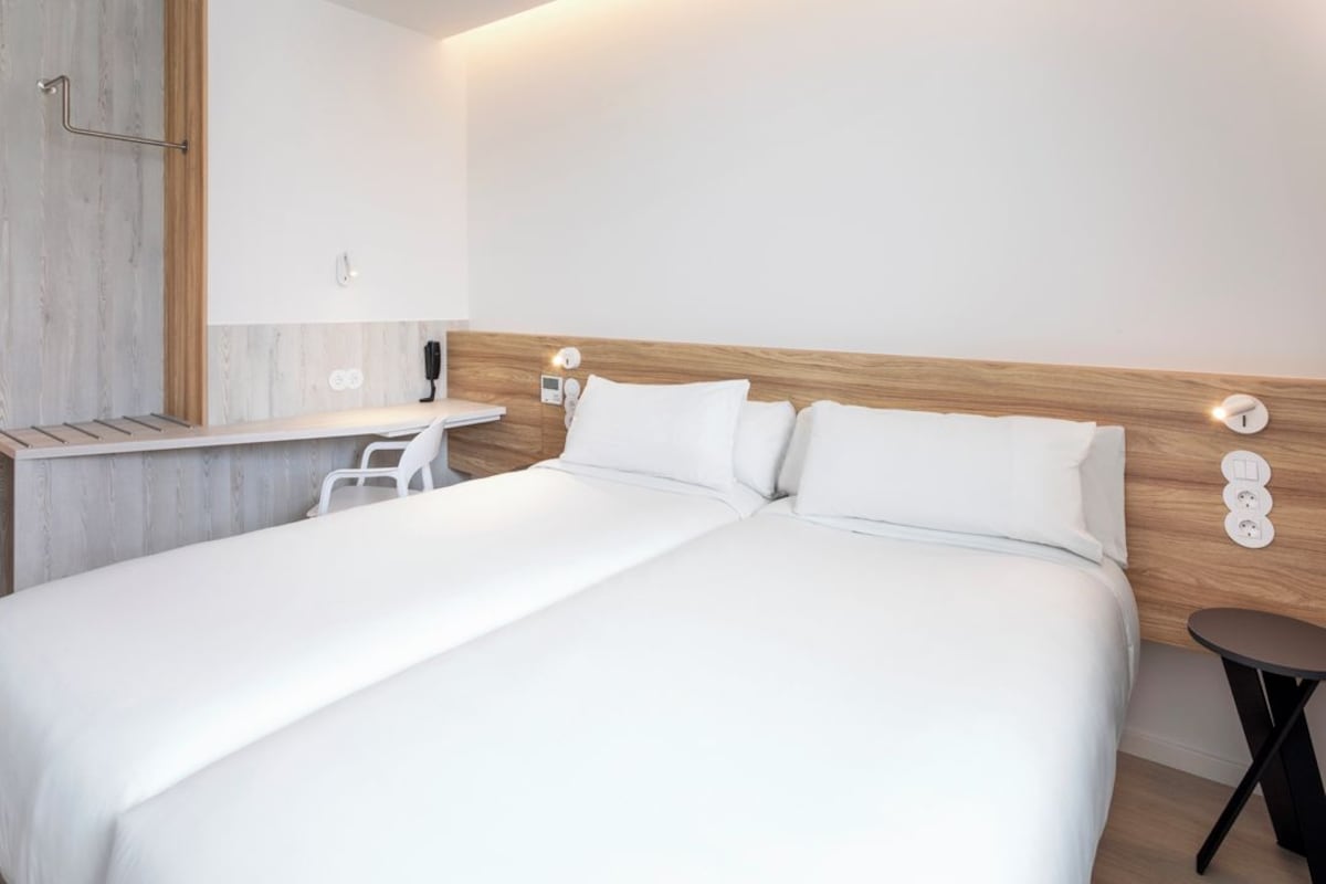 A modern hotel room with a large bed, a small desk, and a chair.