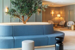 Un área de descanso moderna con un sofá azul, una mesita, una lámpara y una planta decorativa.