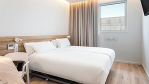 A modern hotel room with a wooden headboard, a bed with white linens, a bedside table, and a window with curtains. - B&B Hotel Vila Do Conde (Vila do Conde)