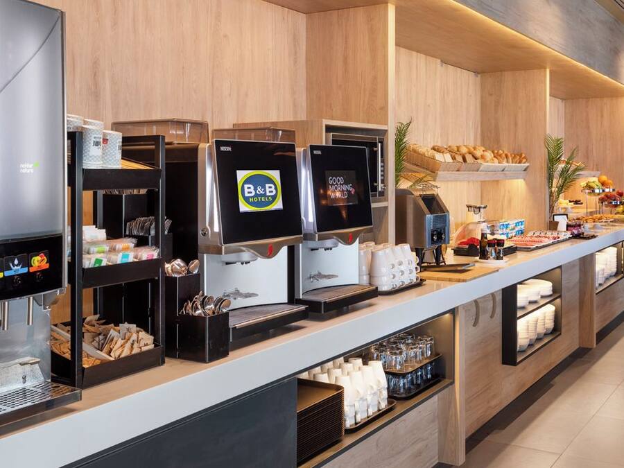 A B&B hotel breakfast area with coffee machines, a fruit display, and a variety of breakfast items.