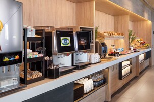 A B&B hotel breakfast area with coffee machines, a fruit display, and a variety of breakfast items.