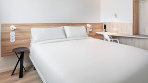 A modern hotel room with a wooden headboard, a single bed, a small round table, and a white chair. - B&B Hotel Vila Do Conde (Vila do Conde)