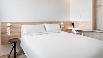 A modern hotel room with a wooden headboard, a single bed, a small round table, and a white chair.