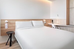 A modern hotel room with a wooden headboard, a single bed, a small round table, and a white chair. - B&B Hotel Vila Do Conde (Vila do Conde)