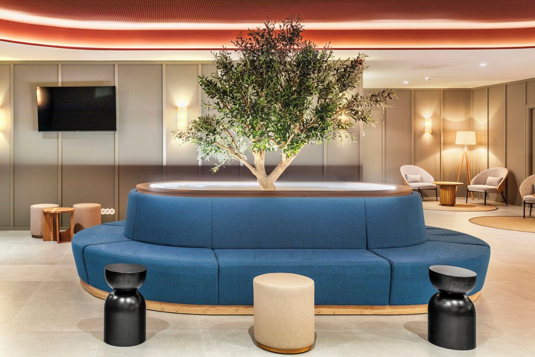 A modern lobby with a blue sofa, a tree planter, and a flat-screen TV.
