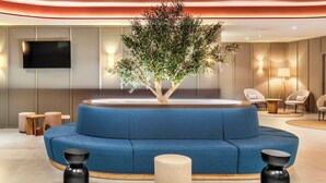 A modern lobby with a blue sofa, a tree planter, and a flat-screen TV. - B&B Hotel Vila Do Conde (Vila do Conde)