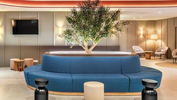 A modern lobby with a blue sofa, a tree planter, and a flat-screen TV.