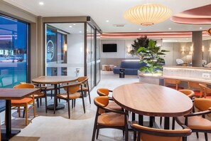 A modern hotel lobby with round wooden tables and orange chairs, a large potted plant, and a bar area. - B&B Hotel Vila Do Conde (Vila do Conde)
