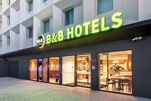 Un hotel con fachada moderna, amplias ventanas de vidrio y un llamativo letrero de neón.