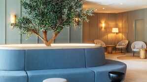 A modern lounge area with a blue sofa, a small table, a lamp, and a decorative tree. - B&B Hotel Vila Do Conde (Vila do Conde)