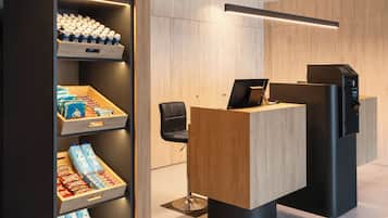 A reception area with a wooden desk, a black chair, and a shelf with bottled water and snacks.