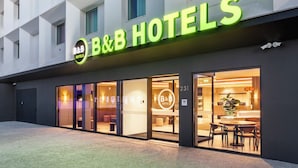 A hotel with a modern facade, large glass windows, and a prominent neon sign. - B&B Hotel Vila Do Conde (Vila do Conde)