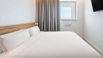 A hotel room with a bed, curtains, a window, and a wall-mounted TV.