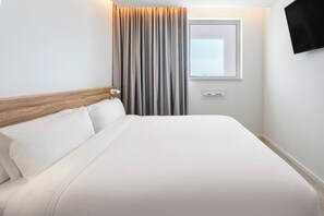 A hotel room with a bed, curtains, a window, and a wall-mounted TV. - B&B Hotel Vila Do Conde (Vila do Conde)