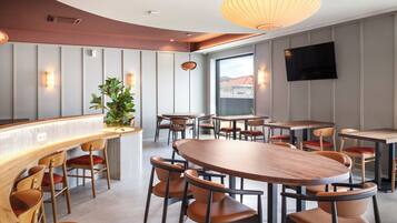 A modern dining area with wooden tables and chairs, a bar counter, and a large window providing a view.