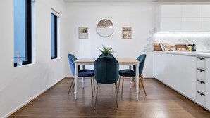Moderni keittiö, jossa on ruokapöytä ja -tuolit, seinällä oleva kello ja ikkunasta avautuva näkymä.