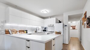 A modern kitchen with white cabinetry, a central island, and a hexagonal tile backsplash. - Riverside 2-bed Apartment With Balcony & Parking (Melbourne)