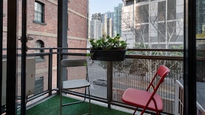 A balcony with two chairs, a small table with a plant, and a view of tall buildings. - Riverside 2-bed Apartment With Balcony & Parking (Melbourne)