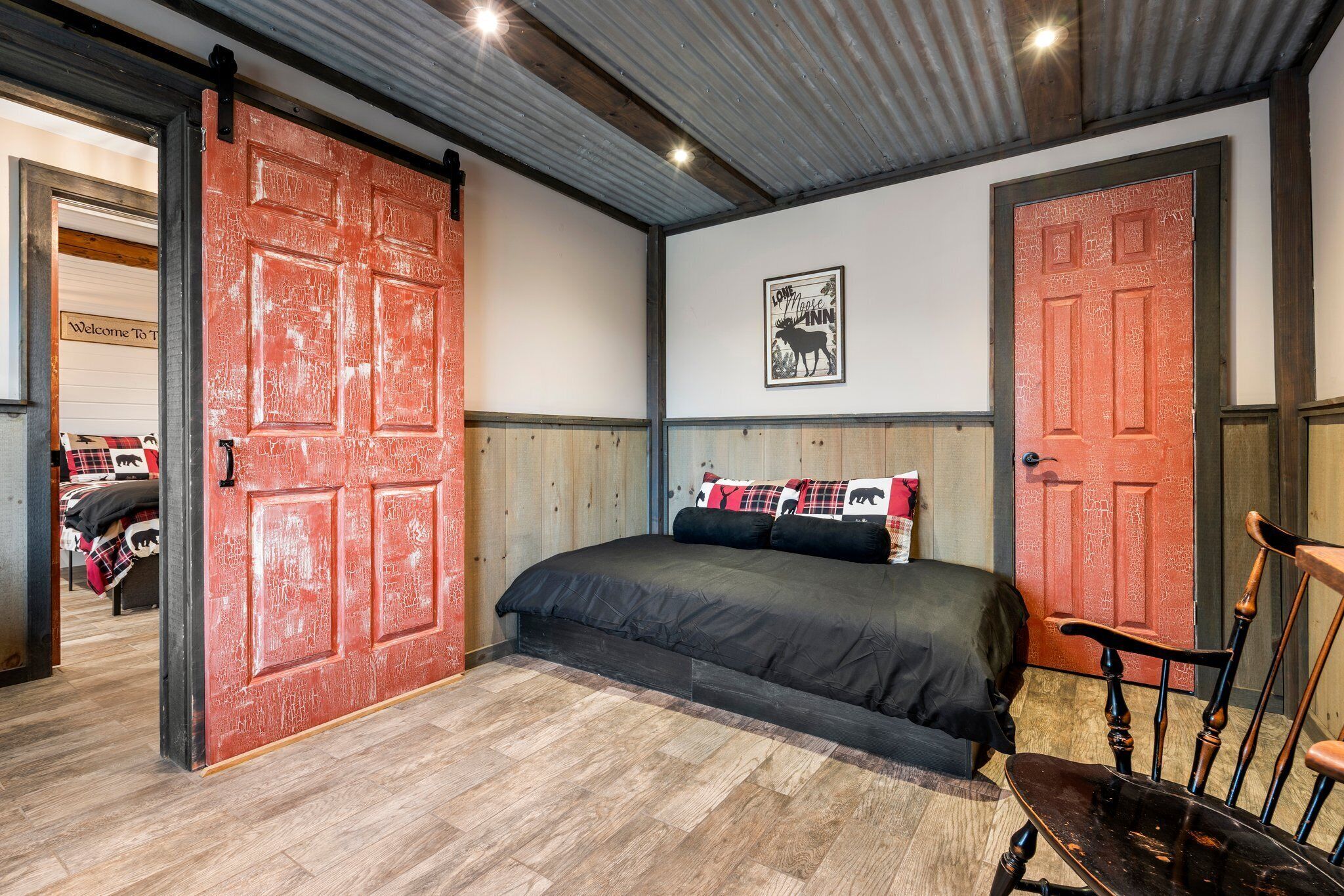 Une chambre à coucher avec un grand lit, deux portes rouges, un plancher en bois et un tableau encadré au mur.