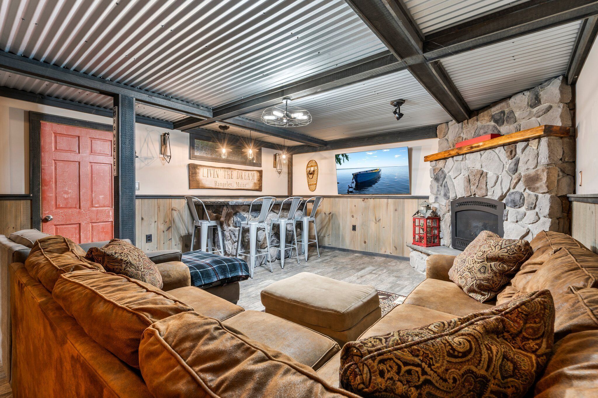 A cozy living room with a stone fireplace, a dining area with chairs, and a red door.