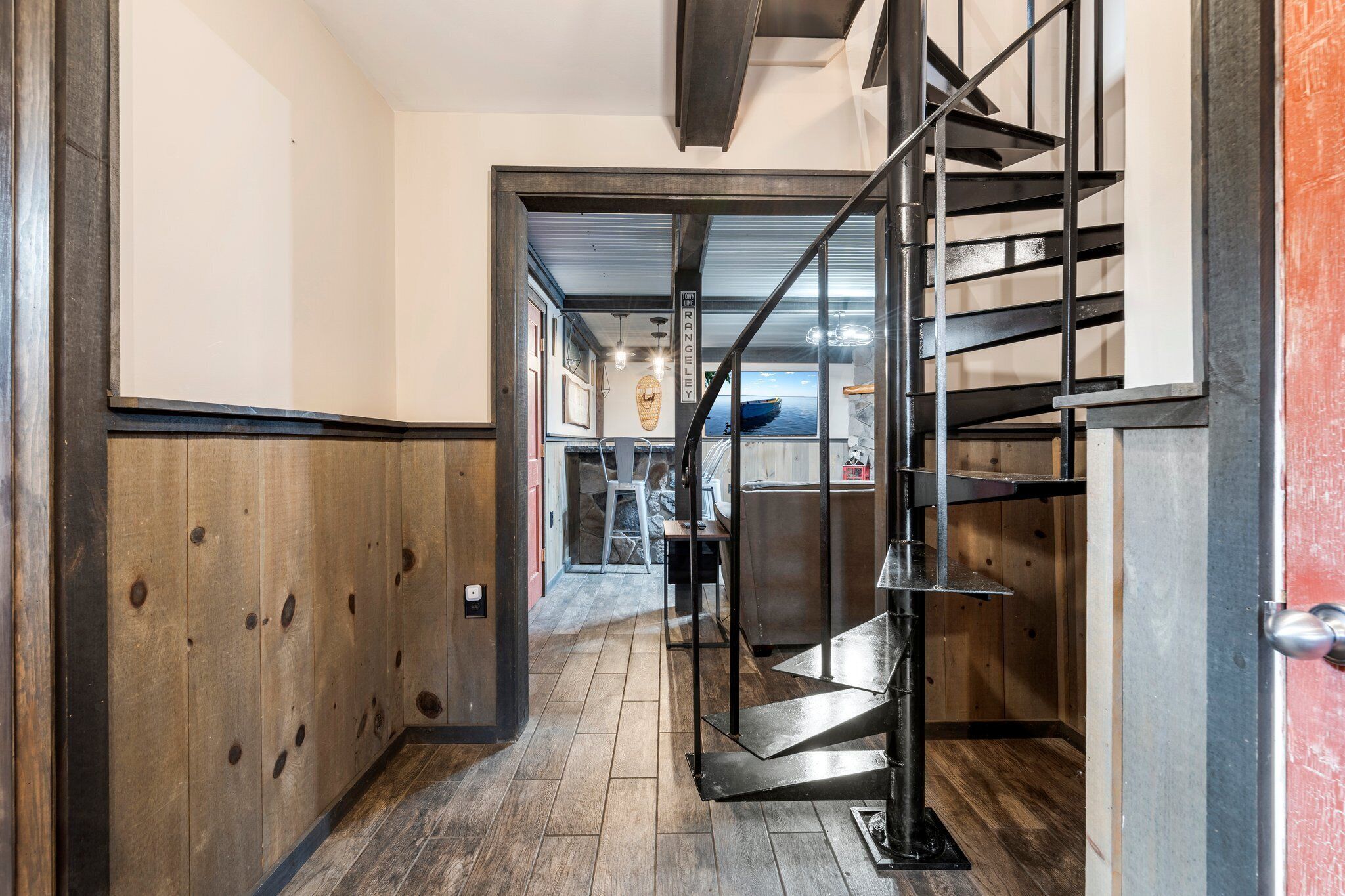A hallway with wooden paneling, a metal staircase, and a view of the sea through a glass door.