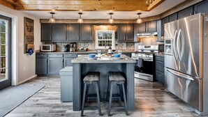 A modern kitchen with dark cabinets, stainless steel appliances, and a central island with bar stools. - S Diamond S Retreat | Huge Backyard & Hot Tub – 2 Miles to Town! (Rangeley)