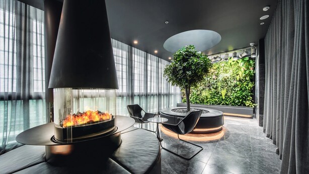 A modern lounge area with a fireplace, seating, and a view of a lush green garden through large windows. - Stylish Southbank 1-bed Flat With Luxury Amenities (Melbourne)