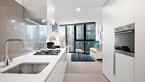 A modern kitchen with a large window, a built-in stove, and a refrigerator. - Stylish Southbank 1-bed Flat With Luxury Amenities (Melbourne)