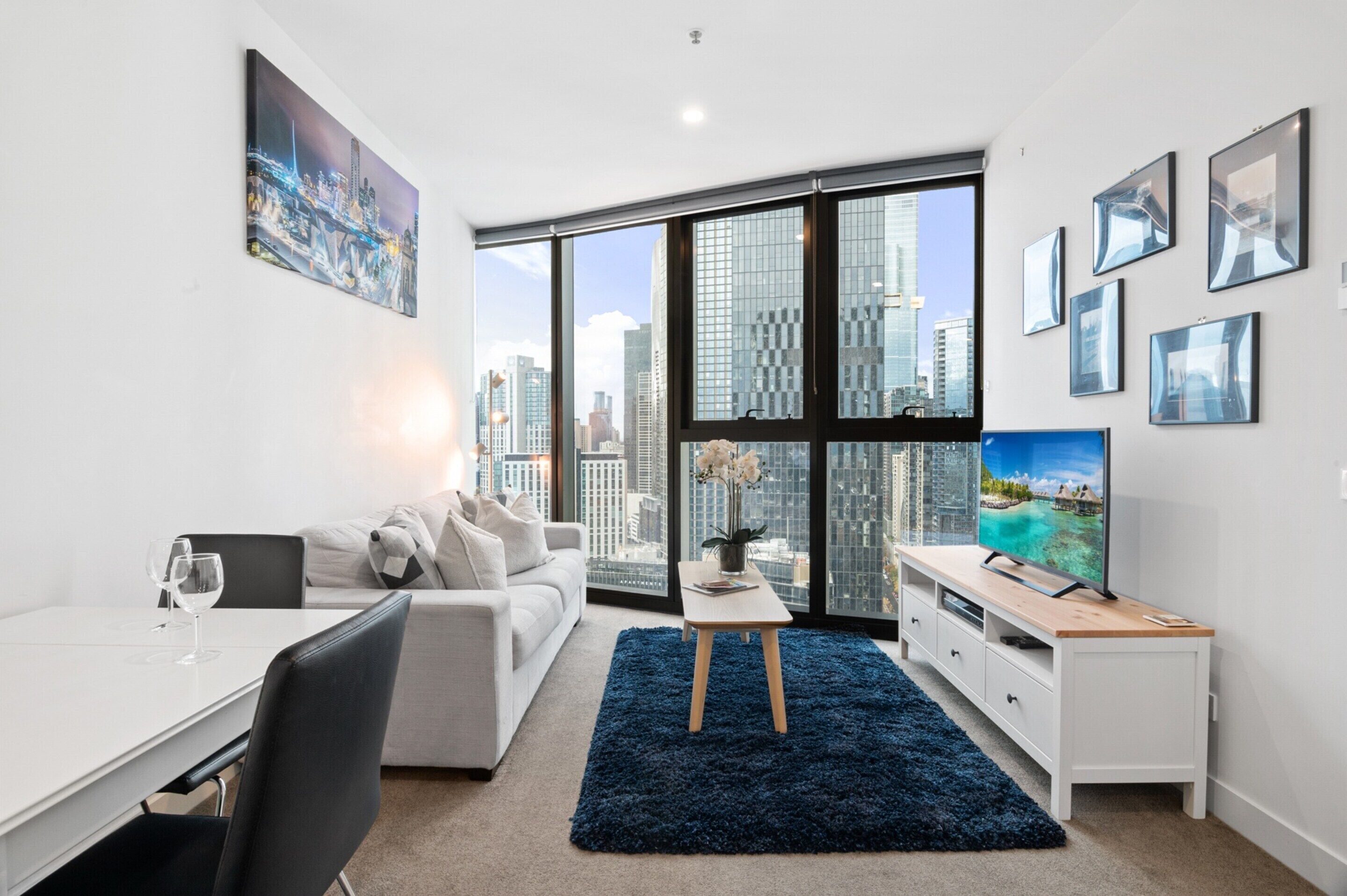 A modern living room with a city view, a dining area, and a TV on a wooden stand.